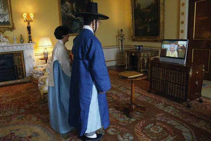 Queen Elizabeth II appears on a screen via videolink from Windsor Castle, where she is in residence, during a virtual audience to receive the Ambassador from the Republic of Korea, Gunn Kim, accompanied by HeeJung Lee (left), at Buckingham Palace, London, October 2021.