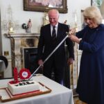 President of The Poppy Factory Surgeon Rear Admiral Lionel Jarvis looks on as Queen Camilla slices a cake with a sword during a celebration at Clarence House, central London, marking the centenary of The Poppy Factory, which was founded in the aftermath o